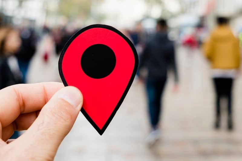 person holding up a map pin in front of a blurred out crowd
